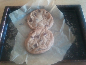2 chocolate chip cookies, on parchment paper atop a toaster oven baking sheet